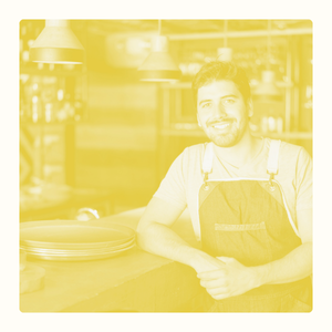 Un homme souriant avec un tablier, posant dans une cuisine lumineuse.