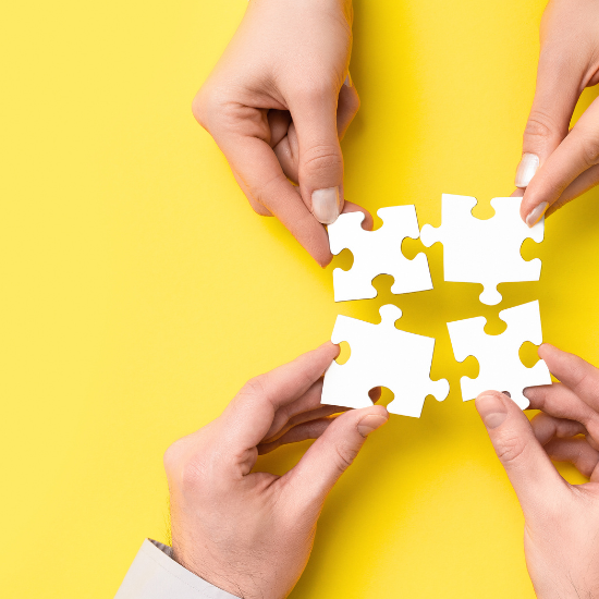 Quatre pièces de puzzle blanches tenues par des mains sur un fond jaune.