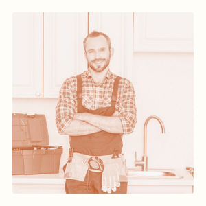 Homme souriant en tablier, bras croisés, dans une cuisine équipée.