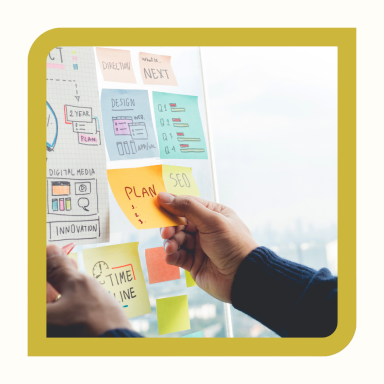 Main dans une chemise sombre plaçant des Post-it colorés sur un tableau.
